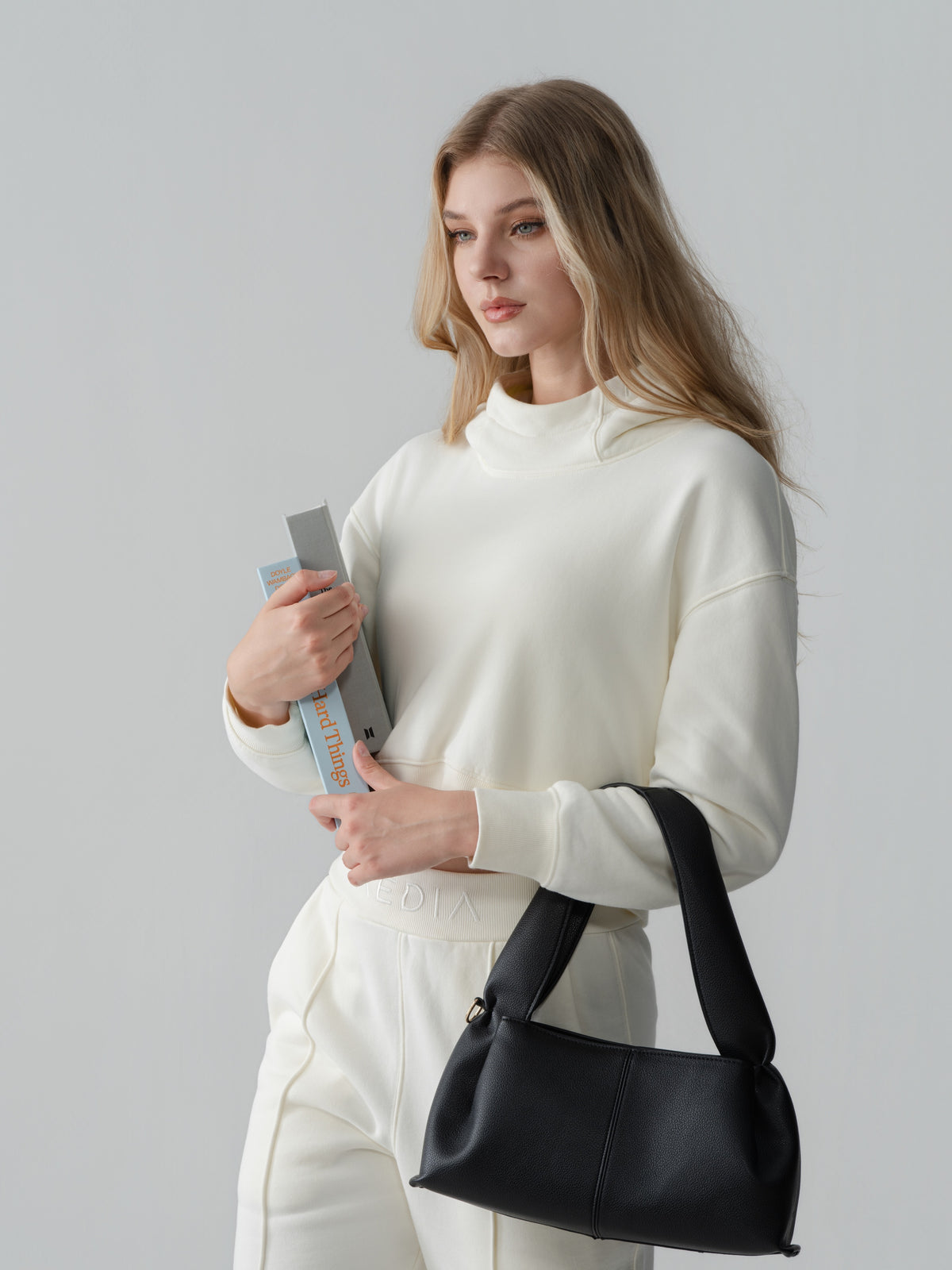Model wearing the AEDIA Funnel Hoodie in Milk with books and a black shoulder bag